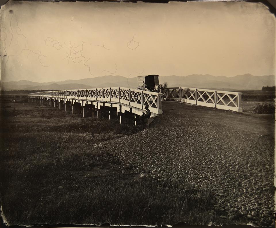 Te Ore Ore Bridge, near Masterton 1876 Large white bridge with gravel ramp in foreground at right. Bragge's cart on bridge, man sits beside bridge on left